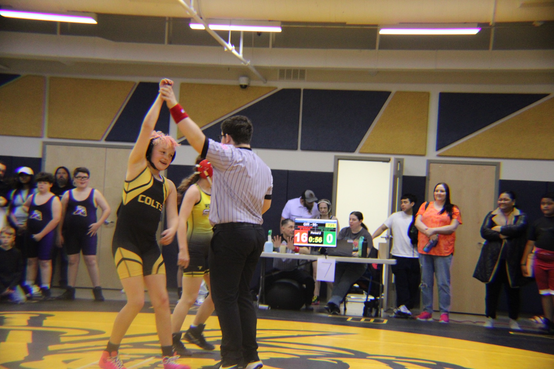 A young Cottonwood wrestler smiling with her hand raised after a match on the Colts mat