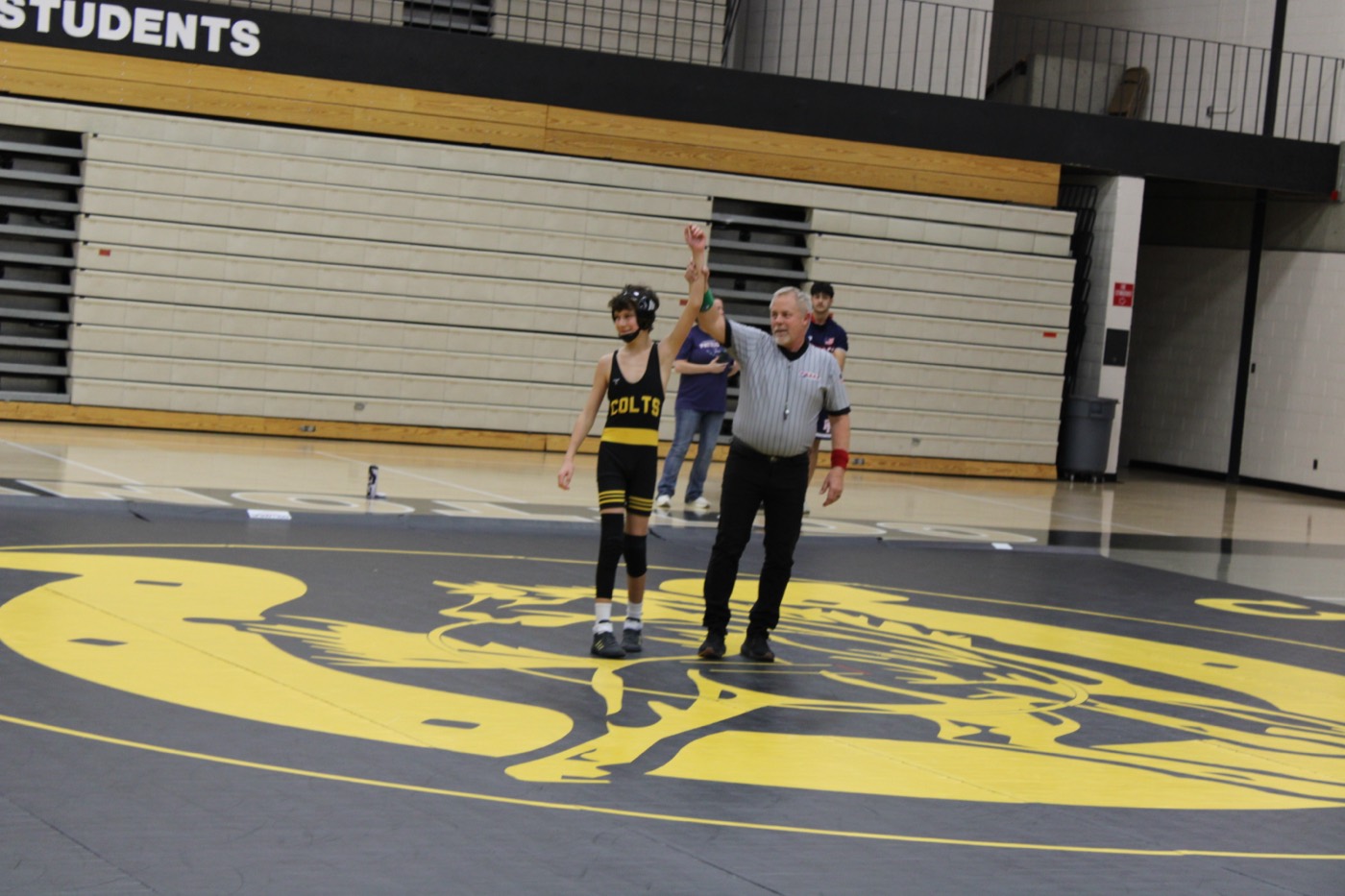 A young Colts wrestler with his hand raised on the Cottonwood mat